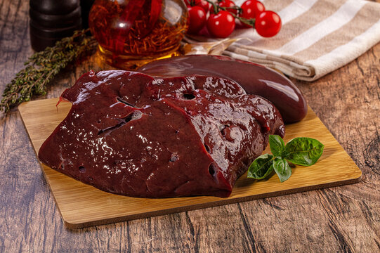 Raw beef liver on wooden cutting board with herbs and tomatoes for cooking