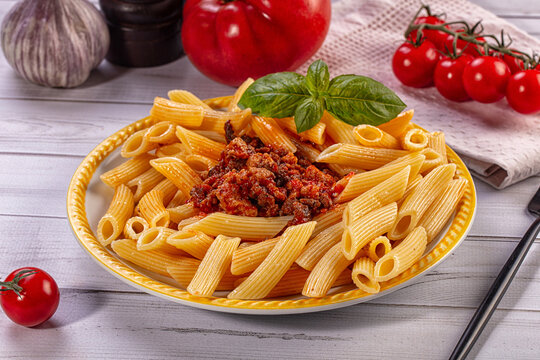 Penne rigati with meat sauce and fresh basil on yellow plate