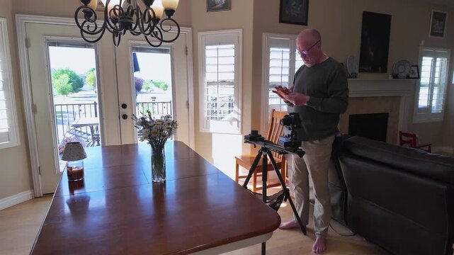 A retired Caucasian man focused on configuring video production equipment and a slider track at home