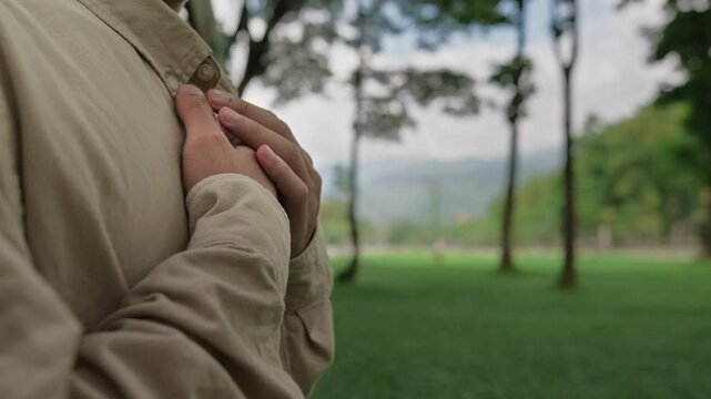 A man holding his hands over his chest in prayer, faith, and deep spiritual connection, feeling inner peace and religious devotion amidst a serene, beautiful nature background.