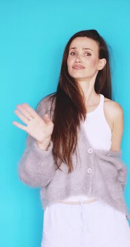 Skeptical young woman saying no and waving hand in refusal, rolling eyes with annoyed facial expression, shaking head in disagreement and disapproval isolated on vibrant blue studio background