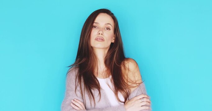 Confident young woman looking directly into camera with proud serious facial expression, crossing arms and posing with calm gaze in cozy grey cardigan isolated on vibrant blue studio background