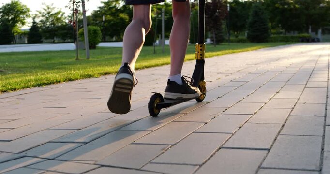 Boy rides scooter along park pathway at sunset. Warm evening light captures simple childhood moments, creating nostalgic atmosphere and lasting memories.