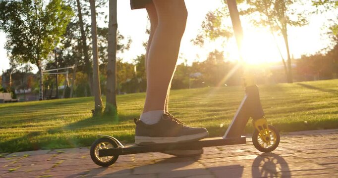 Teenager commuting by scooter through park at sunset highlights eco-friendly transportation choices and sustainable urban mobility in everyday life.