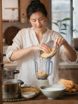 Top 5 chinesische Getr&auml;nke: Junge Frau bereitet chinesische Sojamilch aus Sojabohnen im Mixer zu, serviert mit Youtiao &ndash; authentische Fr&uuml;hst&uuml;cksszene aus der chinesischen K&uuml;che.