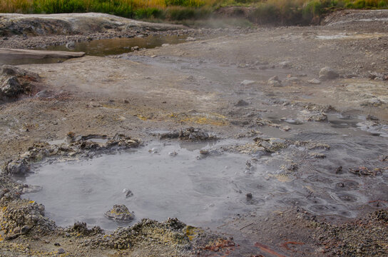 Large bubbling grey mud pot with steam, sulfur deposits and volcanic ground at Dachnye Hot Springs in Kamchatka, Russia.