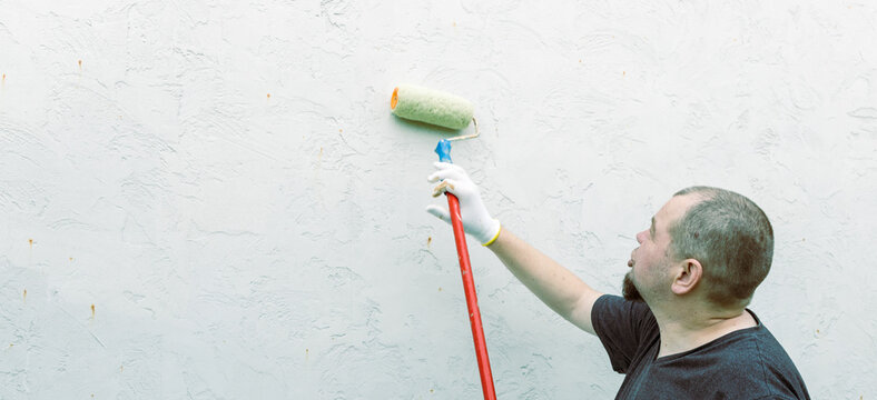 Man paints a plain wall with a roller