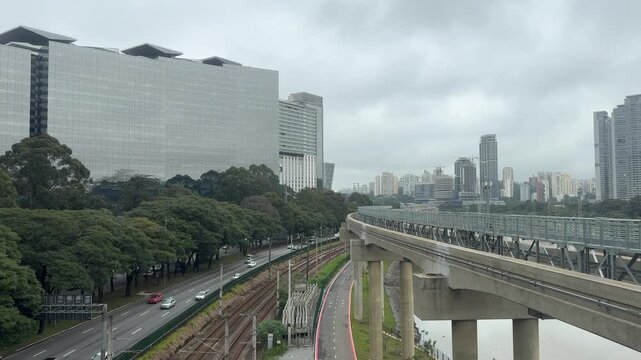 anoramic view of São Paulo's Berrini business district featuring the elevated Line 17 Gold monorail guideway alongside Avenida Nações Unidas (Marginal Pinheiros), metropolitan railway tracks.