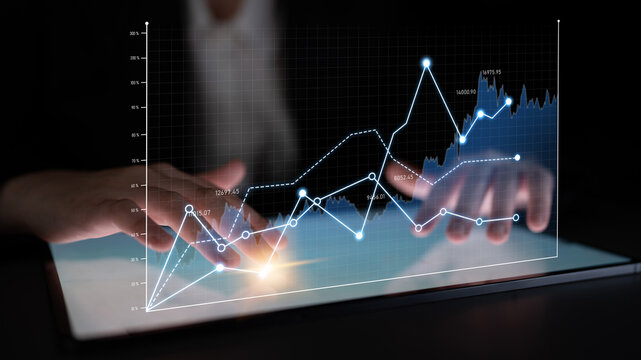 A business professional manipulates digital graphs on a tablet, highlighting data analysis and financial trends in a modern setting. The dark environment enhances the technology theme. Scalp
