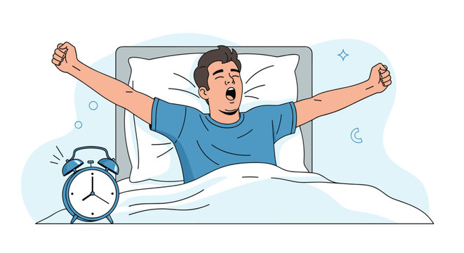 Tired young man yawning and stretching his arms in bed with an alarm clock ringing on the bedside table next to him.
