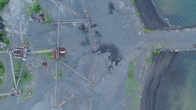 Top Down drone view of black sand aggregate stockpile and coastal industrial site. Ideal quarrying and industrial documentary concepts.