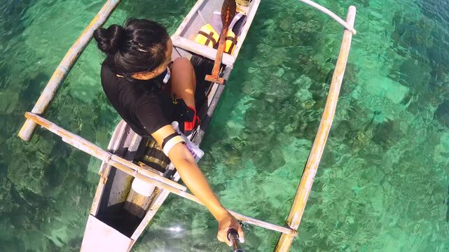 up to bottom side selfie view from a young asian female holding gopro action camera sitting on the small boat looking down to the crystal clear green blue water shallow lagoon through ripple ocean to 
