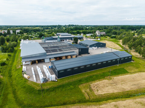Malpils, Latvia - 24 June 2026: Aerial view of a woodworking manufacturing facility with industrial buildings, storage areas, and green fields in the countryside.