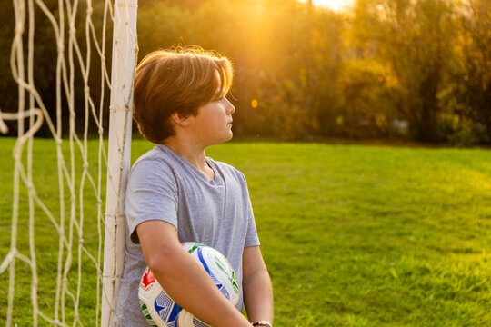 portrait of pre teen boy holding soccer ball on green lawn with net in background