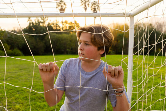 portrait of pre teen boy holding soccer ball on green lawn with net in background