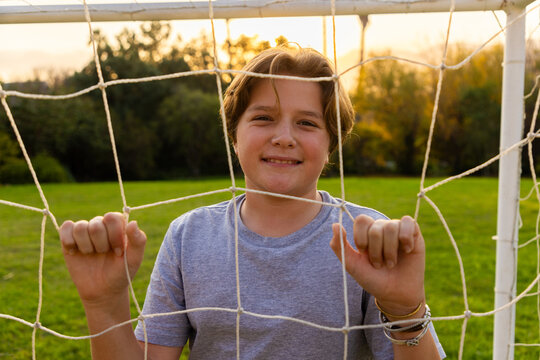 portrait of pre teen boy holding soccer ball on green lawn with net in background
