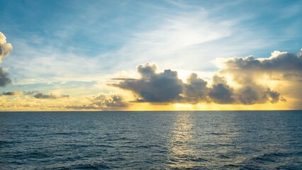 Fototapeta premium Beautiful golden sunrise over calm ocean with dramatic sunbeams breaking through clouds perfect for cruise travel advertising and web banner designs.