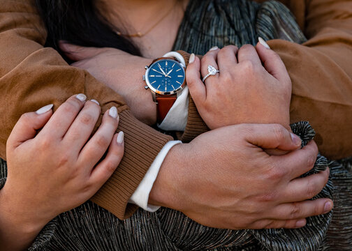 man hugging woman from behind close up of hands embracing with a wristwatch and a dimond ring