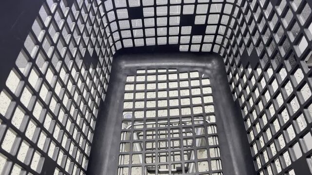 Black plastic laundry basket with a grid pattern is shown from above, revealing its interior structure and design. The sequence highlights the basket's shape and visible details in a clean setting