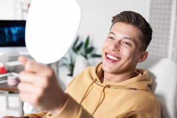 Man looking in mirror at his teeth with dental implant at clinic