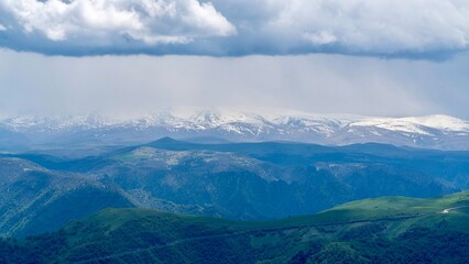 Naklejka premium Dzhily-Su, Russia - June 4, 2026: Scenic view of the Caucasus Mountains on the way to Dzhily-Su, with peaks covered by clouds, misty mountain slopes, overcast sky, and green valleys