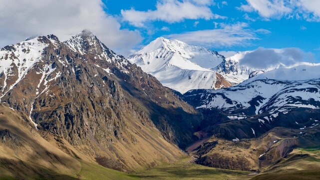 Dzhily Su, Russia - June 4, 2026: Scenic view of snow-covered peaks in the Caucasus Mountains near Elbrus Mountain, with rugged mountain ridges, cloudy weather, highland landscape, and panoramic views