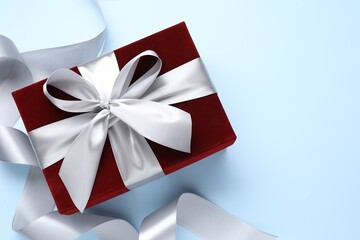 Fototapeta premium Beautiful velvet gift box and ribbon on light blue background, flat lay. Space for text
