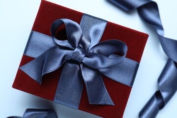 Fototapeta premium Beautiful velvet gift box and ribbon on light blue background, flat lay