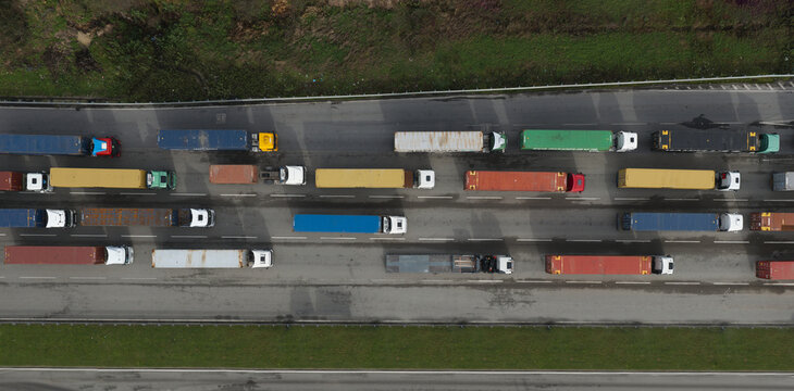 Portugal - 24 June 2026: Aerial view of a line of semi-trucks carrying colorful shipping containers on a highway, with green grass verges on either side.