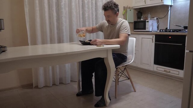 Simple morning dining. Individual delights in basic kitchen setting. Person savors breakfast in kitchen environment. Casual scene of man enjoying his morning meal in humble apartment kitchenette