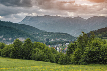 Obraz premium Kolasin mountain valley featuring a small village, green forests and meadows under a dramatic cloudscape, Montenegro