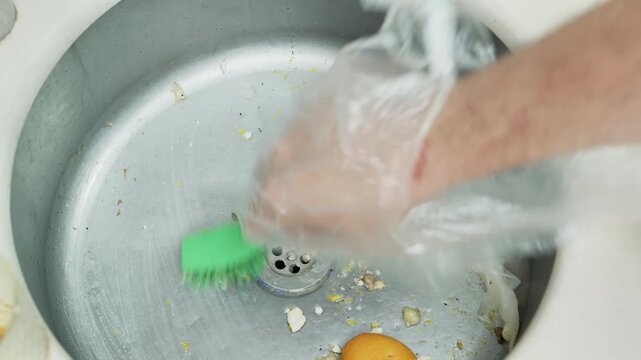 Gloved Hand Scrubbing Food Waste from Kitchen Sink