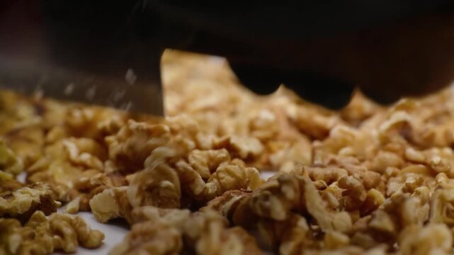 High-angle macro footage of a chef or baker preparing a sweet walnut tart, showing a thick layer of rich, golden-brown walnut kernels being leveled or pressed. The scene highlights the crunchy texture