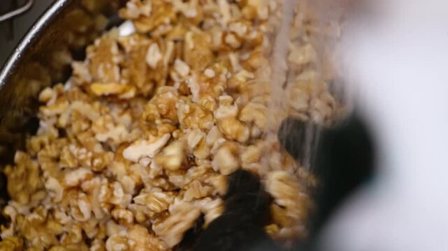 High-angle close-up of a person wearing black gloves washing a large batch of raw, shelled walnut halves in a metal bowl. This preparation step removes tannins and bitterness, ensuring a sweet and but