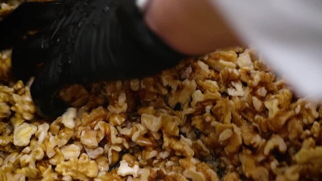 Close-up footage of a baker wearing black protective gloves washing a large batch of shelled walnut kernels in water. This preparation step ensures clean, high-quality ingredients for baking gourmet w