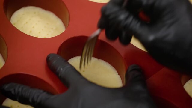 A professional pastry chef wearing black nitrile gloves carefully works with a dessert mixture inside a red silicone mold, focusing on precision and artisan technique in a commercial kitchen setting.