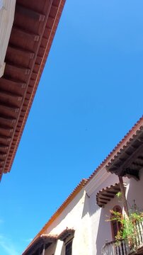 A low angle view looking up at historic Spanish colonial buildings with wooden balconies and lush green plants against a clear blue sky in Walled City Cartagena Colombia