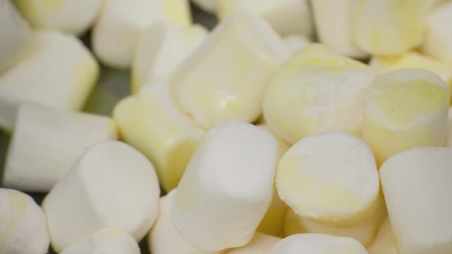 A detailed close-up shot capturing white and yellow cylindrical marshmallows as they begin to melt and soften in a pan. This footage illustrates the gooey, sticky texture essential for creating a mars