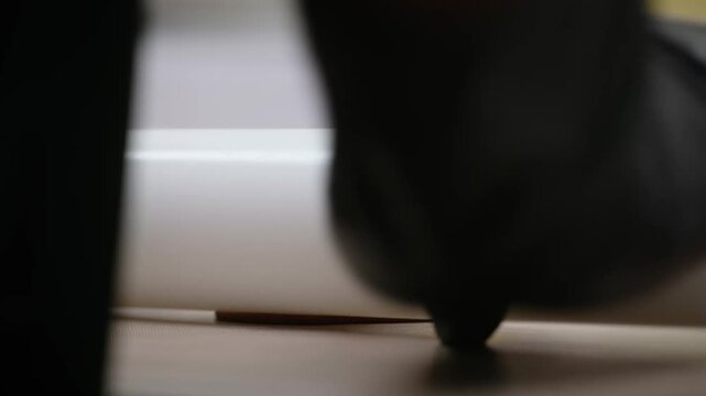 Close-up side view of a professional white dough sheeter machine flattening a thick piece of smooth, reddish-brown pastry dough on a clean surface. The footage captures the precision of industrial bak