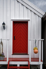 Red door on a white wooden house with nautical decorations, cloudy day © MarekLuthardt