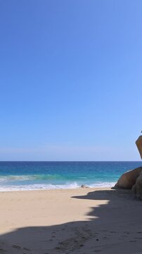Scenic view of powerful ocean waves breaking on a golden sand beach next to dramatic rock cliffs in Cabo San Lucas Mexico