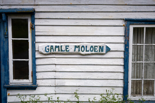 Charming Weathered 'Gamle Moloen' Sign on Rustic White Wall with Blue Trim Windows