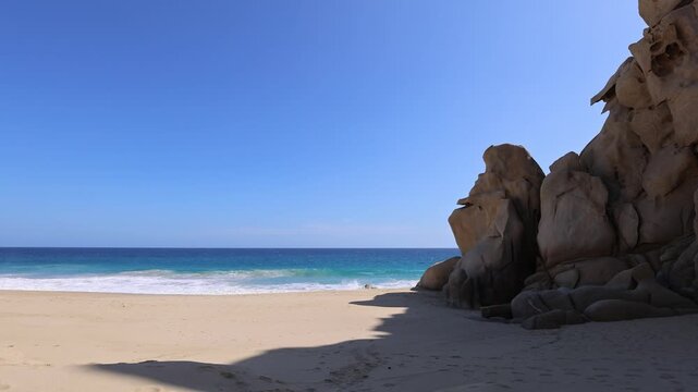 Scenic view of powerful ocean waves breaking on a golden sand beach next to dramatic rock cliffs in Cabo San Lucas Mexico