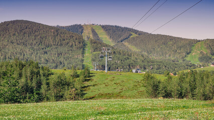 Obraz premium Gondola lift cabins transporting passengers up the Zlatibor mountain, offering scenic views over the vibrant green landscape and forest