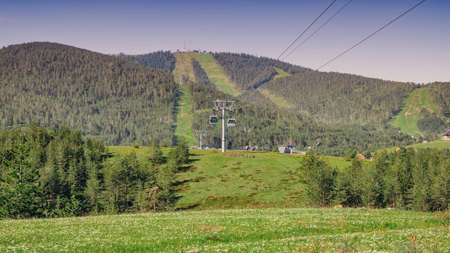 Gondola lift cabins transporting passengers up the Zlatibor mountain, offering scenic views over the vibrant green landscape and forest