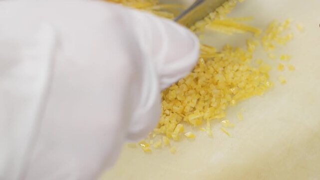 close-up shot of a professional chef wearing white gloves carefully grating fresh organic lemon zest on a white cutting board. The vibrant yellow citrus peel is being prepared as a key aromatic ingred