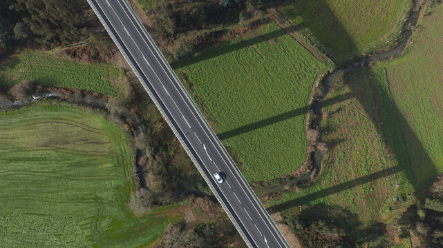 Portugal - 24 June 2026: Aerial view of a tall road viaduct crossing over vibrant green farming fields, a winding stream, and patches of trees in a valley.