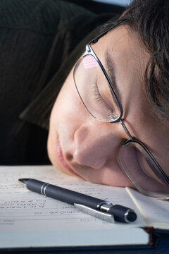 Joven estudiante universitario exhausto durmiendo sobre sus apuntes de estudio