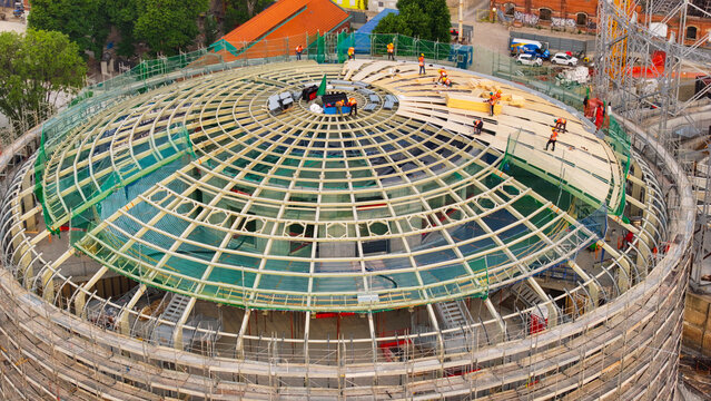 Aerial view of a circular building under construction with a complex dome roof structure and workers in safety gear in Milan, Lombardy, Italy.