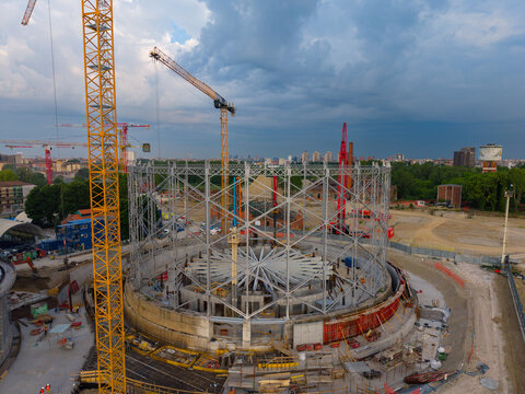 Aerial view of the restoration of the historic gasometer featuring a large circular metal framework and multiple yellow construction cranes in Milan, Lombardy, Italy.